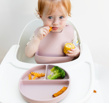 Baby eating corn and pasta with mess-free silicone bib and divided plate, easy clean, food-safe design