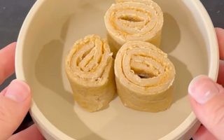 Hands holding a bowl with three rolled-up peanut butter and banana snacks, ideal for mess-free meals.