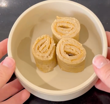 Hands holding a bowl with three rolled-up peanut butter and banana snacks, ideal for mess-free meals.