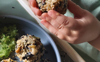 Child's hands holding sesame-coated rice ball over plate, mealtime mess-free with catch tray