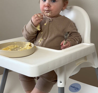 Baby eating messy meal in high chair with Catchy floor mat protecting flooring from food spills
